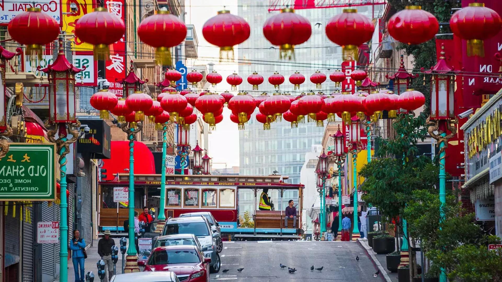 Une rue vallonnée du 邻里中国 de San Francisco est représentée avec des lanternes rouges suspendues et un tramway qui passe.