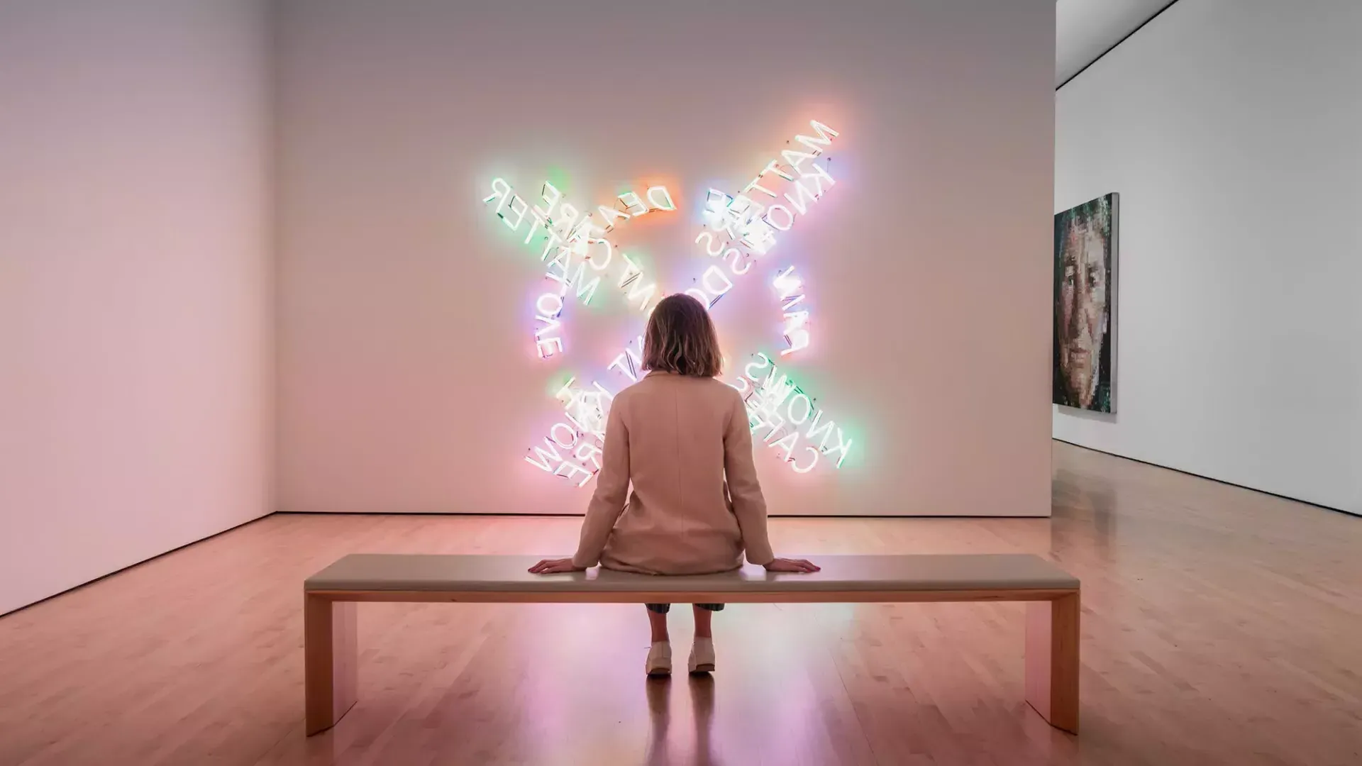 一个女人, 坐在长凳上, guarda un'opera d'arte luminosa contemporanea al SF MOMA di San Francisco.