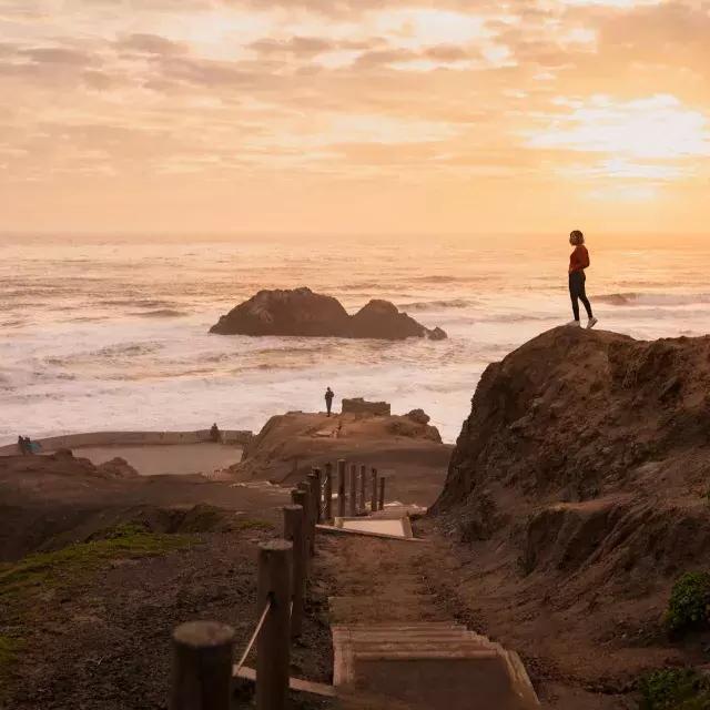 샌프란시스코의 수트로 배스(Sutro Baths)에서 바다가 내려다보이는 바위 위에 두 사람이 서 有了.